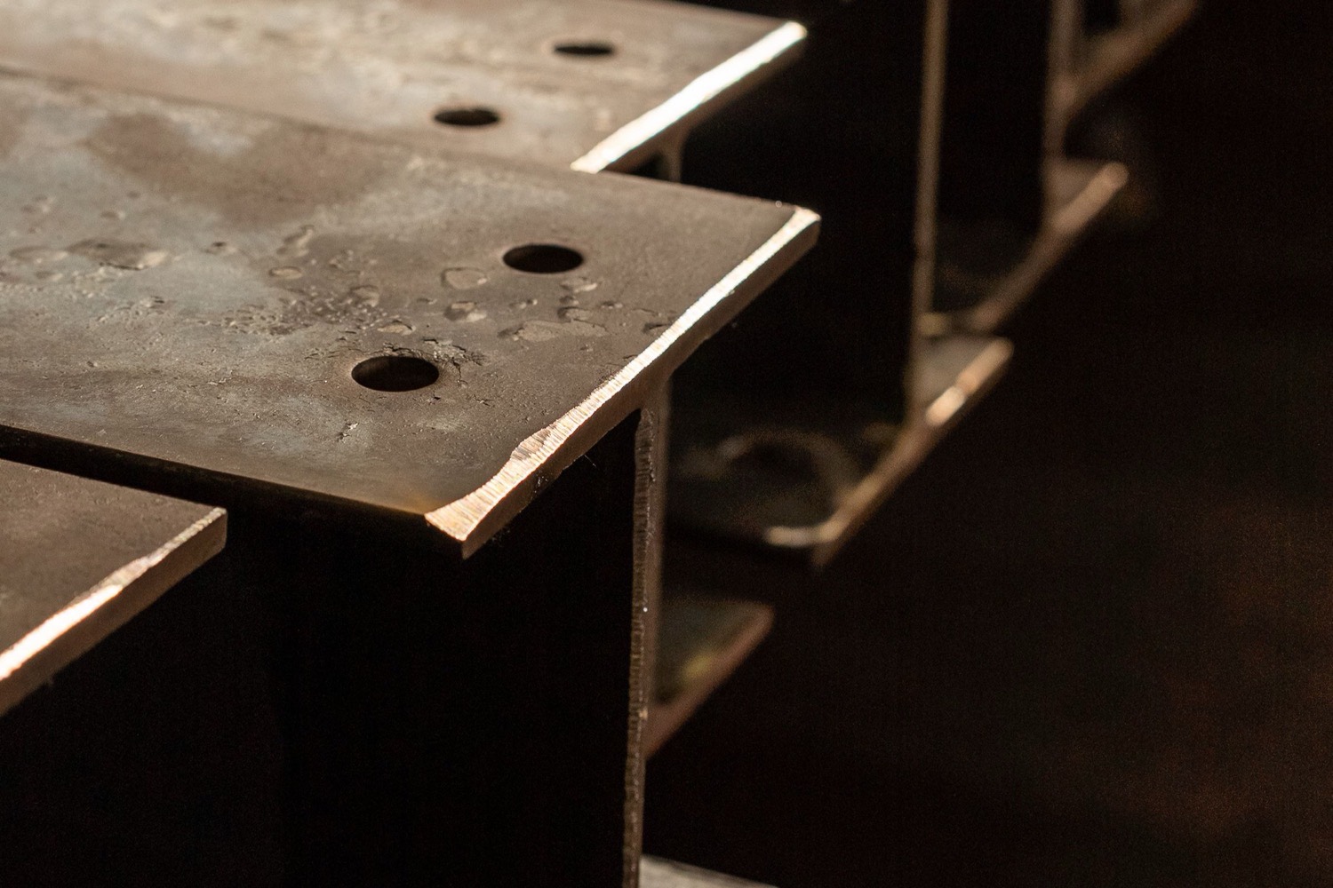 Fabricated structural steel beams with drilled connection holes stacked in a fabrication shop